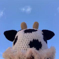 a crocheted cow hat with ears and feathers on it's head, against a blue sky