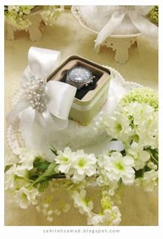 an open box with a ring on top of it surrounded by white flowers and greenery