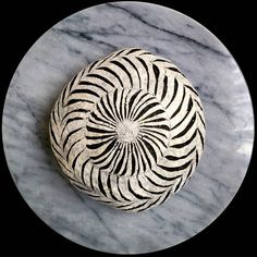 a white and black vase sitting on top of a marble countertop next to a circular object