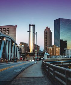 the city skyline is lit up at night, with tall buildings in the background and a bridge leading to it