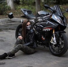 a woman sitting on the ground next to a motorcycle