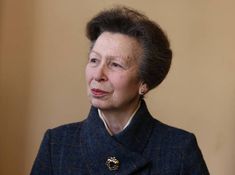 an older woman wearing a blue coat with a gold brooch on her left ear