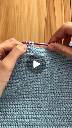 two hands crochet together to make a knitted bag with yarn and buttons