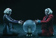 two women sitting on the ground in front of a crystal ball with their hands together