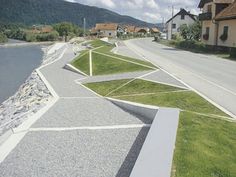 an empty street next to a river with houses on the other side and mountains in the background