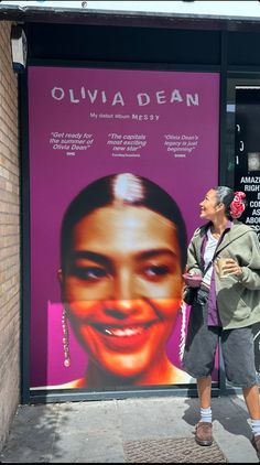 a woman standing in front of a poster on the side of a building that says, ollivia dean