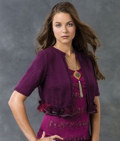 a beautiful young woman standing in front of a gray background wearing a purple top and jeans