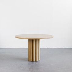 a round wooden table sitting on top of a cement floor next to a white wall