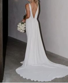 a woman in a white dress holding a bouquet and looking at the back of her gown