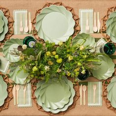 the table is set with green plates, silverware and greenery in vases