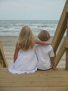 two children sitting on the steps looking out at the ocean