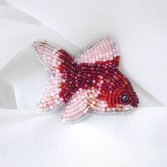 a red and white fish brooch sitting on top of a white cloth