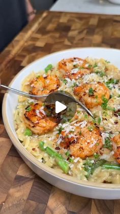 a white bowl filled with pasta and shrimp on top of a wooden table next to a fork