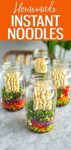 four mason jars filled with pasta and vegetables in them on top of a marble counter