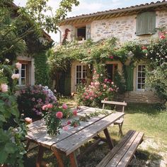 a table and bench in front of a house with roses on the windows, flowers everywhere