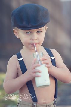 a young boy drinking milk from a glass with a straw in it's mouth