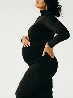 a pregnant woman posing for the camera in a black body - contoured dress