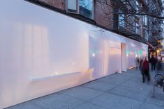 people are walking down the sidewalk in front of a building with white walls and windows