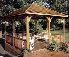 a wooden gazebo sitting on top of a patio next to a lush green field