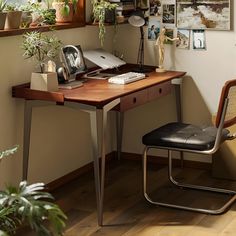 a desk with plants and pictures on the wall above it, along with a chair