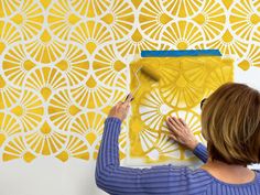 a woman is painting on a wall with yellow and white designs in front of her