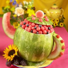 a green tea pot filled with fruit and flowers on a pink cloth covered tablecloth