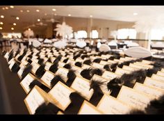 rows of tables with place cards and feather centerpieces at a wedding reception in an elegant setting