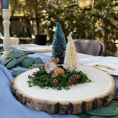 a table topped with a wooden slice covered in greenery and a small deer figurine