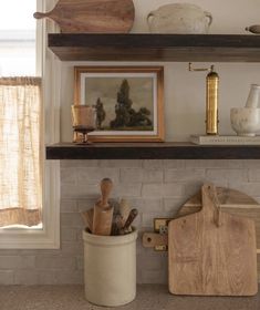 a kitchen shelf filled with wooden utensils and cutting boards next to a window