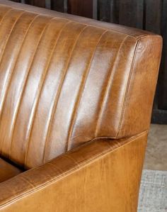 a brown leather couch sitting on top of a carpeted floor next to a wooden wall