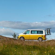 a yellow van parked on top of a grass covered hill