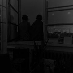 two people are sitting on a window sill looking out at the city skyline in black and white