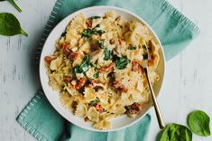 a white bowl filled with pasta and spinach on top of a blue napkin next to a