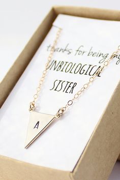 a gold necklace with a triangle on it sitting in a box next to a card