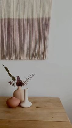 two vases with flowers sit on a wooden table in front of a wall hanging