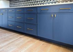 a kitchen with blue cabinets and gold pulls on the doors, wood flooring and white walls