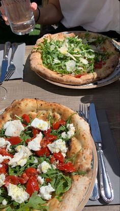 two pizzas sitting on top of a table next to silverware and water glasses