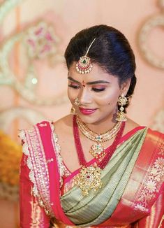 a woman in a red and green sari with gold jewelry on her head, looking down