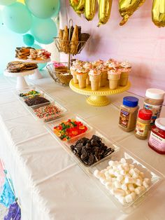 a table topped with lots of desserts next to balloons and confetti cones