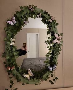 a person taking a photo in a mirror with flowers and leaves on the wall behind it