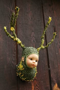 a doll is wearing a knitted hat and scarf with yellow flowers on it's head