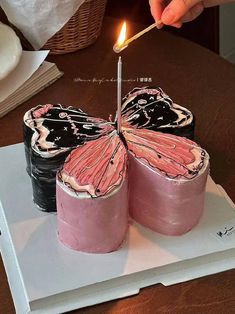 a person lighting a candle on top of a cake with pink and black icing