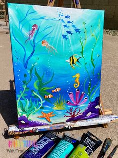 an easel with paint and brushes on it in front of a painting that is under water