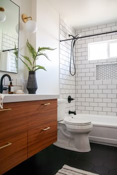 a white toilet sitting next to a bath tub under a window in a bathroom with black and white tiles on the walls