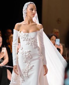 a woman in a white wedding dress and veil walking down the runway at a fashion show