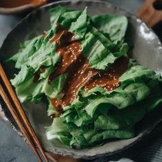 lettuce with sauce and chopsticks in a bowl on top of a table