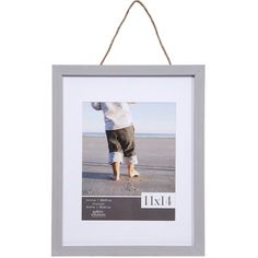 a photo hanging on a rope with a person walking in the sand behind it,