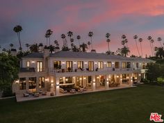 a large white house sitting on top of a lush green field next to palm trees