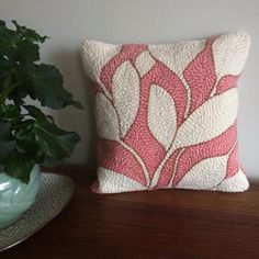 a pink and white pillow sitting on top of a wooden table next to a potted plant