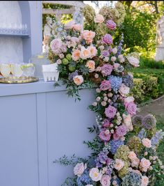 an arrangement of flowers on the side of a white wall in front of a house